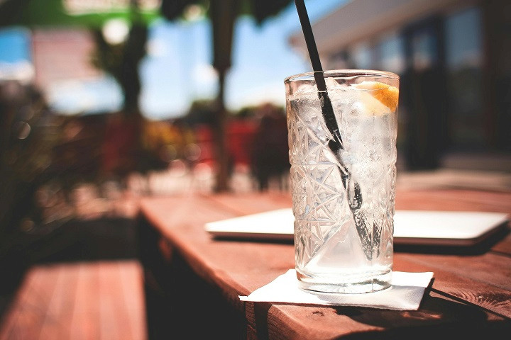 Ein mit Gin gefülltes Glas mit Strohhalm auf einem braunen Holztisch