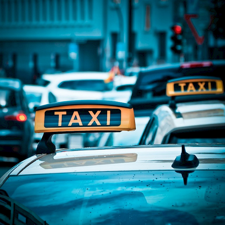 Zwei Taxen stehen vor einer roten Ampel an einer vielbefahrenen Kreuzung