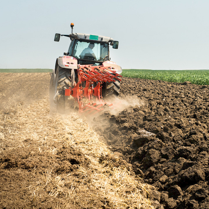 Ein Traktor pflügt einen Ackerboden unter einem klarem Himmel